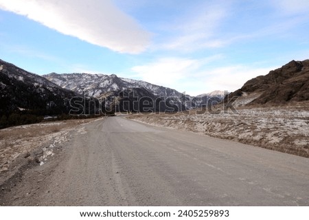 The junction of dirt and asphalt roads in a picturesque winter valley surrounded by snow-capped mountains. Altai, Siberia, Russia.