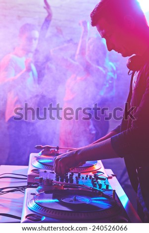 Young deejay adjusting sound on background of group of dancing friends