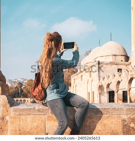 Woman taking photos of Sanliurfa city, mosque and lake with sacred fish- travel, tourism concept in Turkey