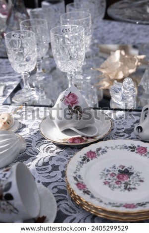 Antique crockery with floral pattern and glassware displayed on a decorated tablecloth at an antique market Royalty-Free Stock Photo #2405299529