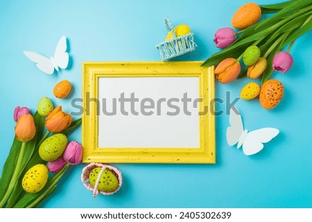 Easter holiday picture frame mock up  with easter eggs and tulip flowers on blue background. Top view, flat lay