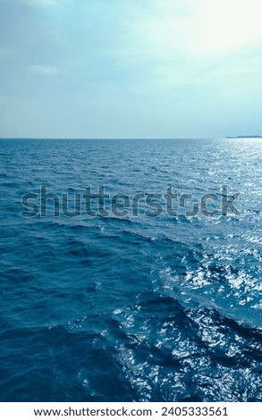 This serene photo captures the calm sea during daylight. Deep blue waters merge with the bright sky.