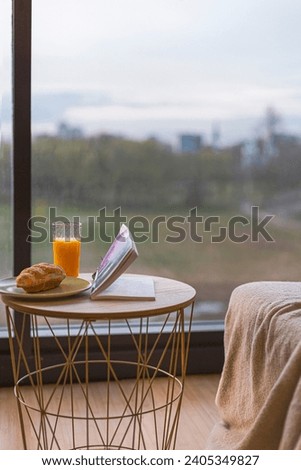 breakfast on the terrace. breakfast on the table with glass of orange juice and book on the table. balcony view of city. city as background. soft sofa. wooden table with metal case. good morning. meal