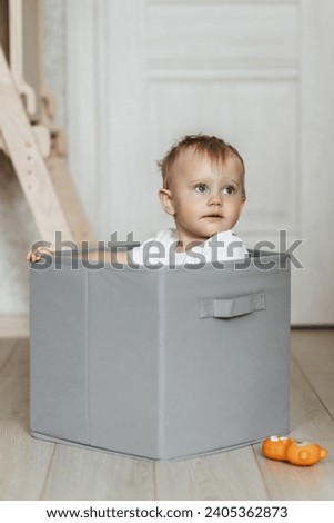 Cute little baby boy sitting inside box with big boxes full of toys on background, moving out concept.