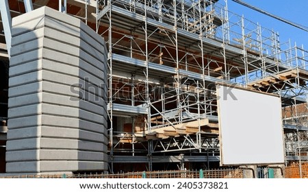 Blank information board hanging on the scaffoldings, by side of concrete foundation for crane in the construction site.  Background for copy space.