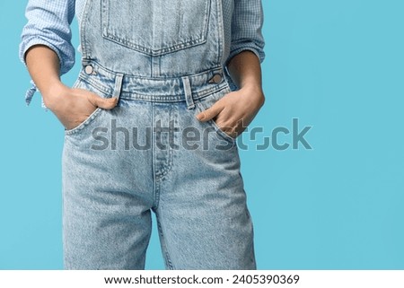 Beautiful young Asian woman in stylish denim jumpsuit on blue background, closeup Royalty-Free Stock Photo #2405390369