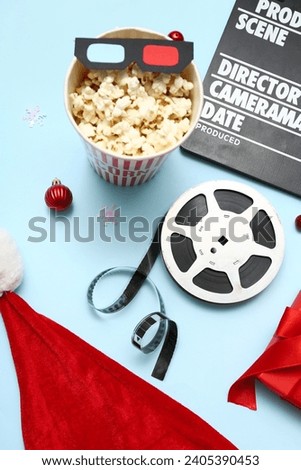 Movie clapper with bucket of popcorn, film reel and Christmas decor on blue background