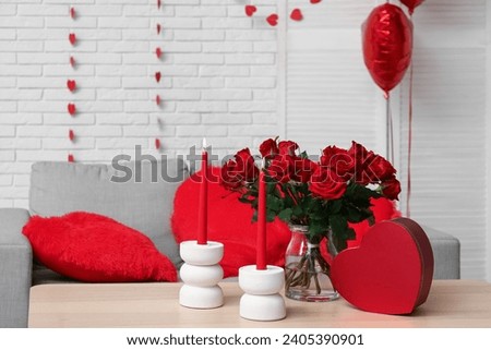 Bouquet of beautiful roses with gift box and candles on table in room decorated for Valentine's Day celebration Royalty-Free Stock Photo #2405390901