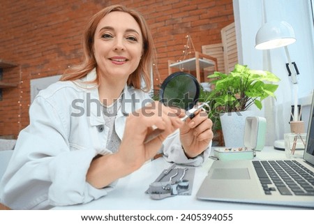 Female jeweler with magnifier examining ring at table in workshop