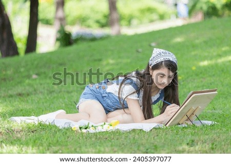 Asian teenage girl drawing a picture in the park with easel, palette, and paintbrush