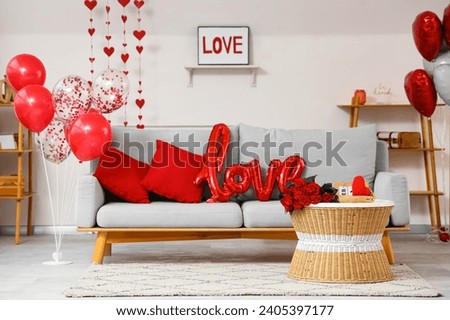 Interior of festive room with grey sofa, word LOVE made from balloons and bouquet of roses on coffee table. Valentine's Day celebration Royalty-Free Stock Photo #2405397177