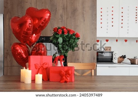 Burning candles, gift boxes and bouquet of roses on wooden table in kitchen, closeup. Valentine's Day celebration Royalty-Free Stock Photo #2405397489