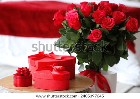 Bouquet of beautiful roses and gift boxes on pouf in bedroom, closeup. Valentine's Day celebration