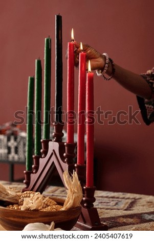 Hand of young unrecognizable African American woman igniting candles on candleholder while preparing for celebration of Kwanzaa