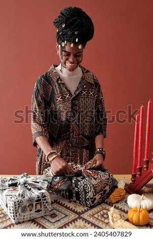 Young smiling African American woman tying knot on packed and wrapped giftbox while preparing Kwanzaa presents for her family