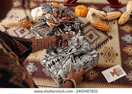 Above angle of young African American woman tying knot on top of packed and wrapped giftbox on table with ears of corn