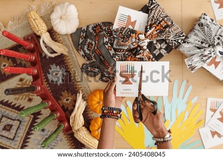 Hands of young woman with scissors cutting part of handmade postcard while creating new one for member of her family or friend
