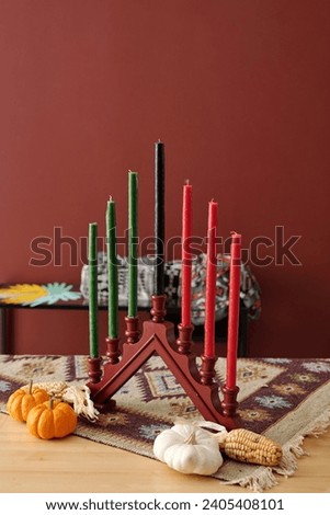 Candlestick with seven multi-colored candles and ripe vegetables standing on table in front of camera before celebration of Kwanzaa