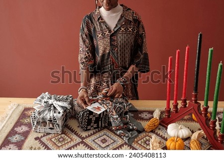 Cropped shot of African American girl putting handmade postcard in giftbox wrap while preparing presents for her family