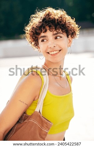 Young beautiful smiling hipster woman in trendy summer clothes. Carefree woman with curls hairstyle, posing in the street at sunny day. Positive model outdoors. Cheerful and happy