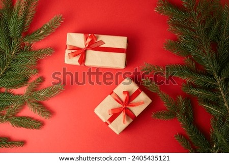 The gift is wrapped in brown craft paper and tied with a red ribbon. On a red background with green Christmas tree branches.