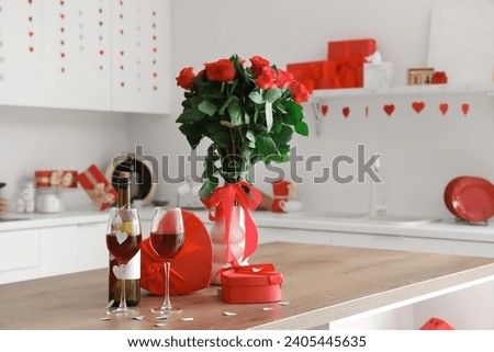 Glasses of wine, gift boxes and bouquet of roses on wooden table in kitchen, closeup. Valentine's Day celebration Royalty-Free Stock Photo #2405445635