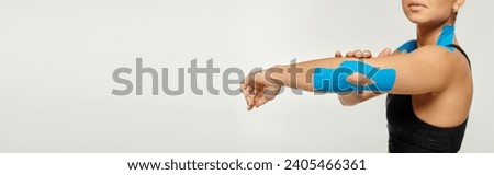 beautiful young woman with kinesiological tapes on her elbow and shoulders on gray backdrop, banner