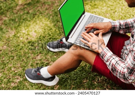 Man typing on grey laptop in park. Concept of working and learning on laptop with green screen and space for text