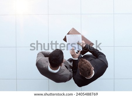 Two businessman signing an agreement. One hand holds the document and the other signs.