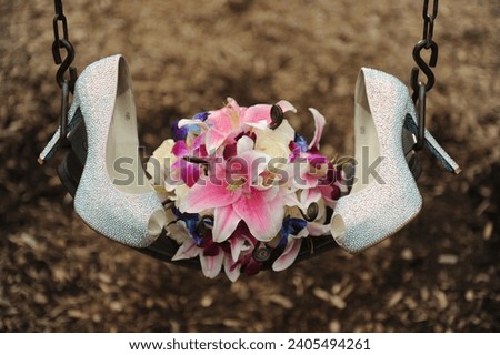 close up of wedding bouquet and white high heels sitting on swing at the park on wedding day Royalty-Free Stock Photo #2405494261