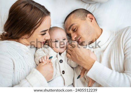 Above, portrait and happy parents with baby on bed for love, care and quality time together at home. Smile of mother, father and family with cute newborn kid relax in bedroom, support and happiness.