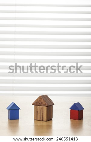 Three houses(made in wood block, red and blue) on the wood office desk(table) behind white blind.