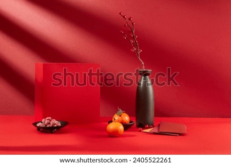 Close-up of a red gift box, a plate of jam, tangerines, lucky money envelopes and a vase of flowers. Empty space for product display. Front view. Royalty-Free Stock Photo #2405522261