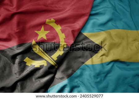 big waving national colorful flag of bahamas and national flag of angola . macro