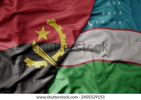 big waving national colorful flag of uzbekistan and national flag of angola . macro