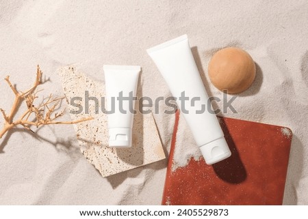 Amidst the white sand background, a wooden branch, wooden ball, unlabeled cosmetic tubes and a notebook stand out. Conveying the natural skincare cosmetics concept.