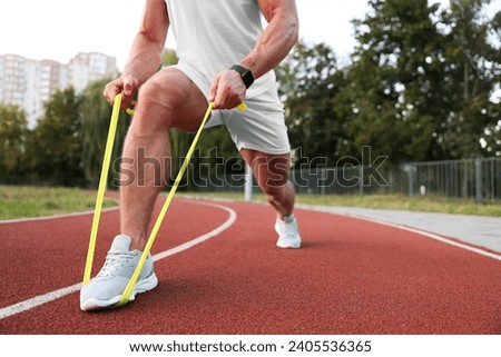 Muscular man doing exercise with elastic resistance band at stadium, closeup