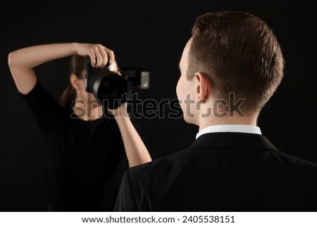 Professional photographer taking picture of man on black background, selective focus