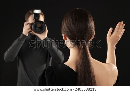 Photographer taking picture of model on black background, selective focus