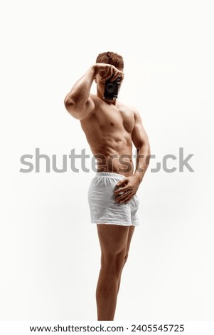 Young guy with muscular relief body, torso standing shirtless in boxers, underwear and taking photo isolated over white studio background. Concept of male beauty, body care, fitness, sport, health