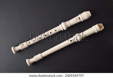 Top and bottom view of two white plastic recorder in diagonal position on black textured table. Top view. Royalty-Free Stock Photo #2405569757
