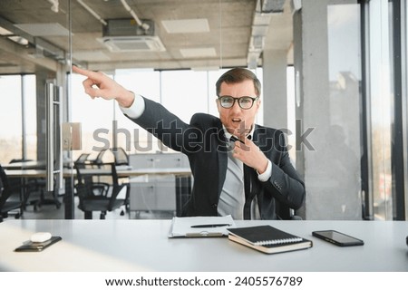 Angry businessman sitting at his desk and screaming at his employees Royalty-Free Stock Photo #2405576789