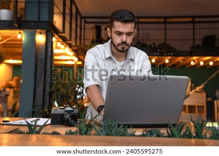 Young businessman photographer video redactor editor using laptop for application online, working remotely in office coworking. Photo camera and equipment