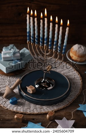 Hanukkah celebration. Menorah with burning candles, dreidels, gift boxes and donut on wooden table