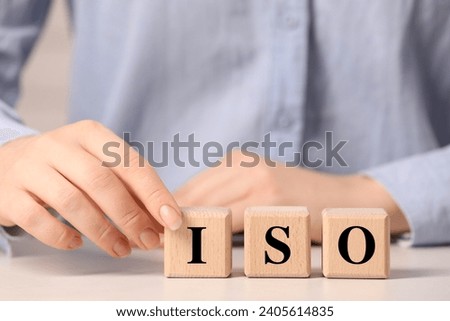 Woman making abbreviation ISO of wooden cubes at white table, closeup