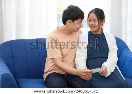pregnant woman with her husband holding some picture and looking each other on sofa
