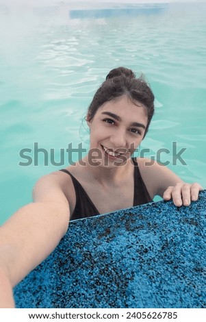 A smiling young dark-haired woman bathes in a hot thermal spring on a winter day.A woman takes pictures of herself on her smartphone.Self-care,healthy lifestyle,leisure activity,mental health concept.