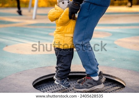 A child toddler in a yellow jacket jumps on a trampoline in the playground in autumn