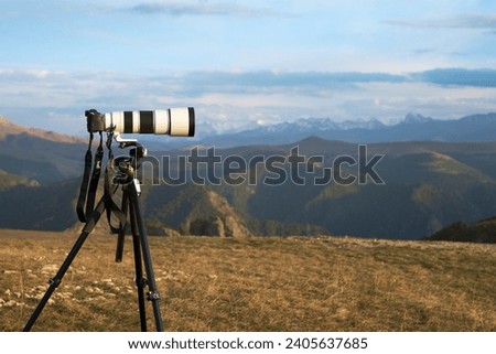 Photography of a distant object at long shutter speed. A camera with a long lens on a tripod against a mountainous terrain. Copy space.                               