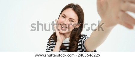 Lifestyle and people concept. Young carefree woman, smiling while taking selfie on smartphone, posing for photo, standing over white background.